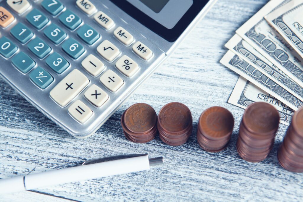 Calculator, stacks of coins, and U.S. dollar bills on a desk, representing retirement calculations and the limitations of using simple rules like the 4% rule for financial planning.